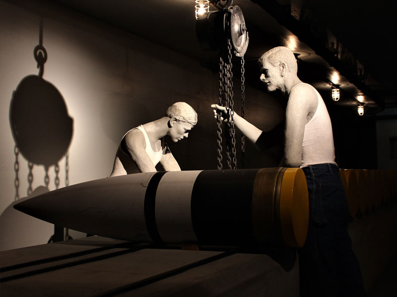 A museum exhibit of two male mannequins pulling chains next to missile.